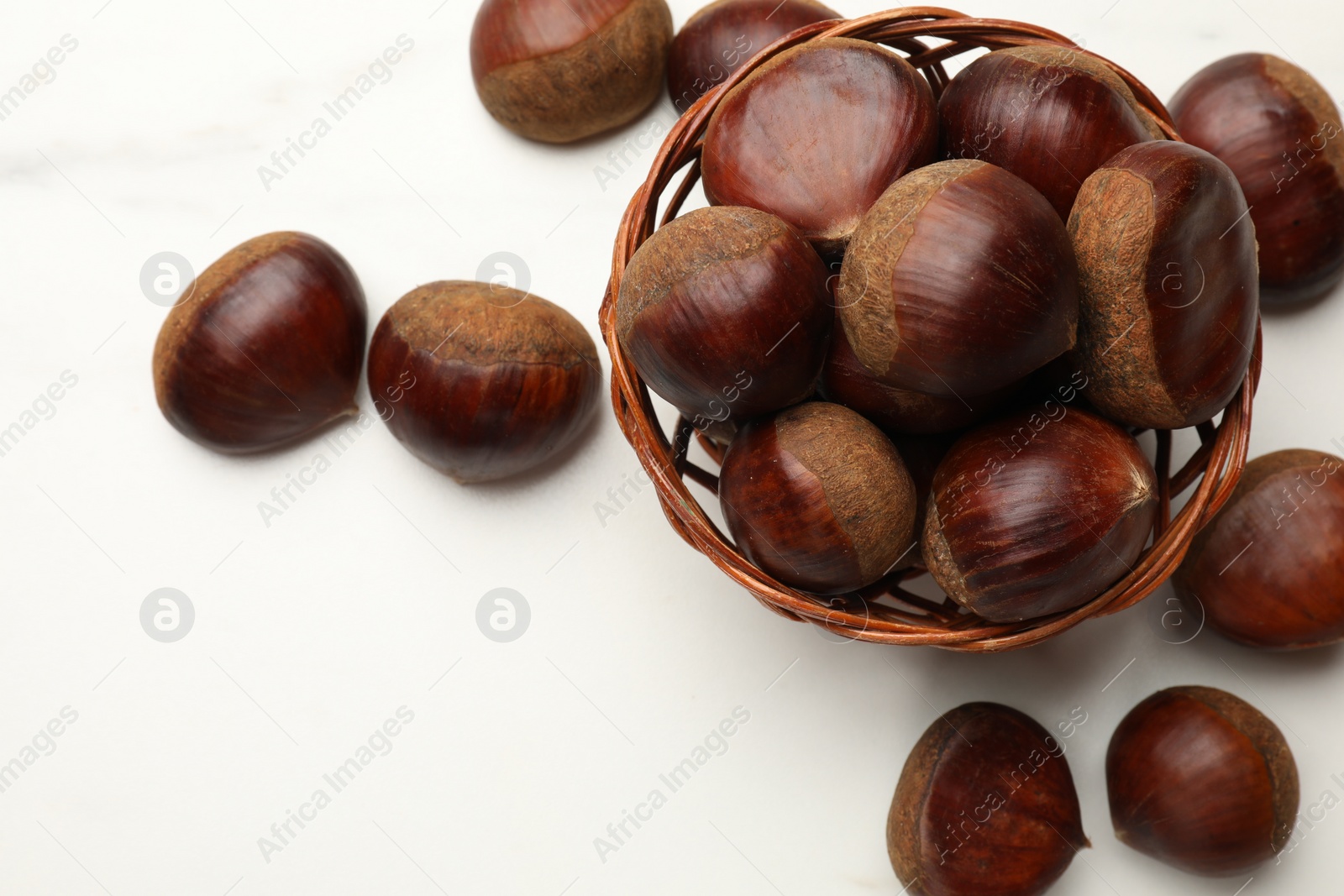 Photo of Sweet fresh edible chestnuts in wicker bowl on white table, top view. Space for text