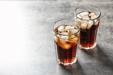Glasses of cola with ice on grey background, space for text