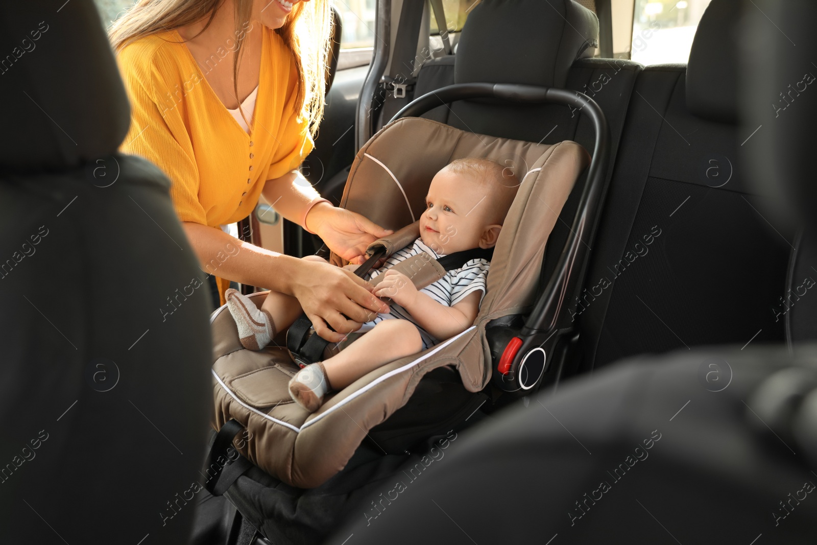 Photo of Mother fastening baby to child safety seat inside of car