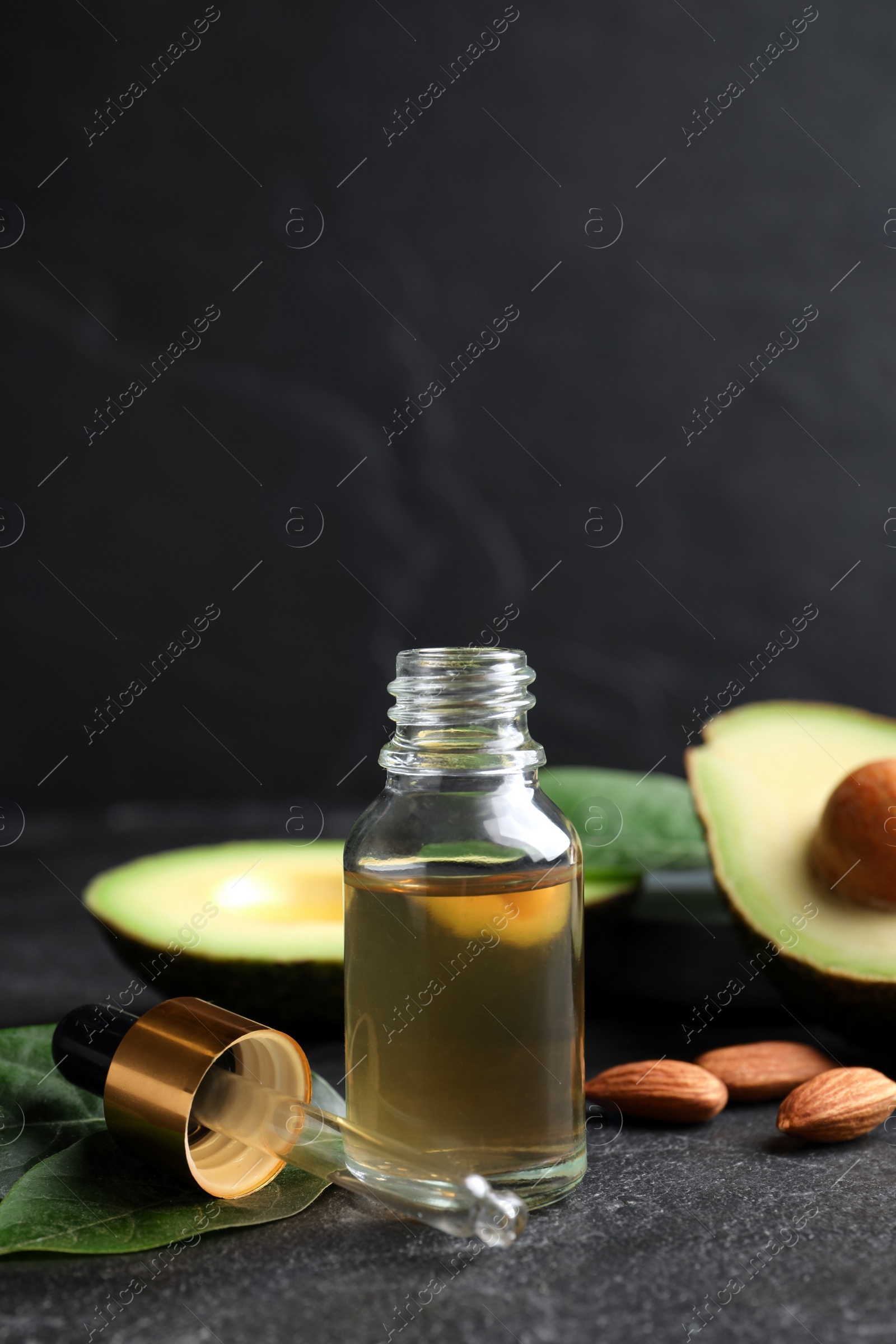 Photo of Essential oil, avocado and almonds on black table. Space for text