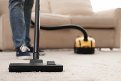 Young man using vacuum cleaner at home, closeup