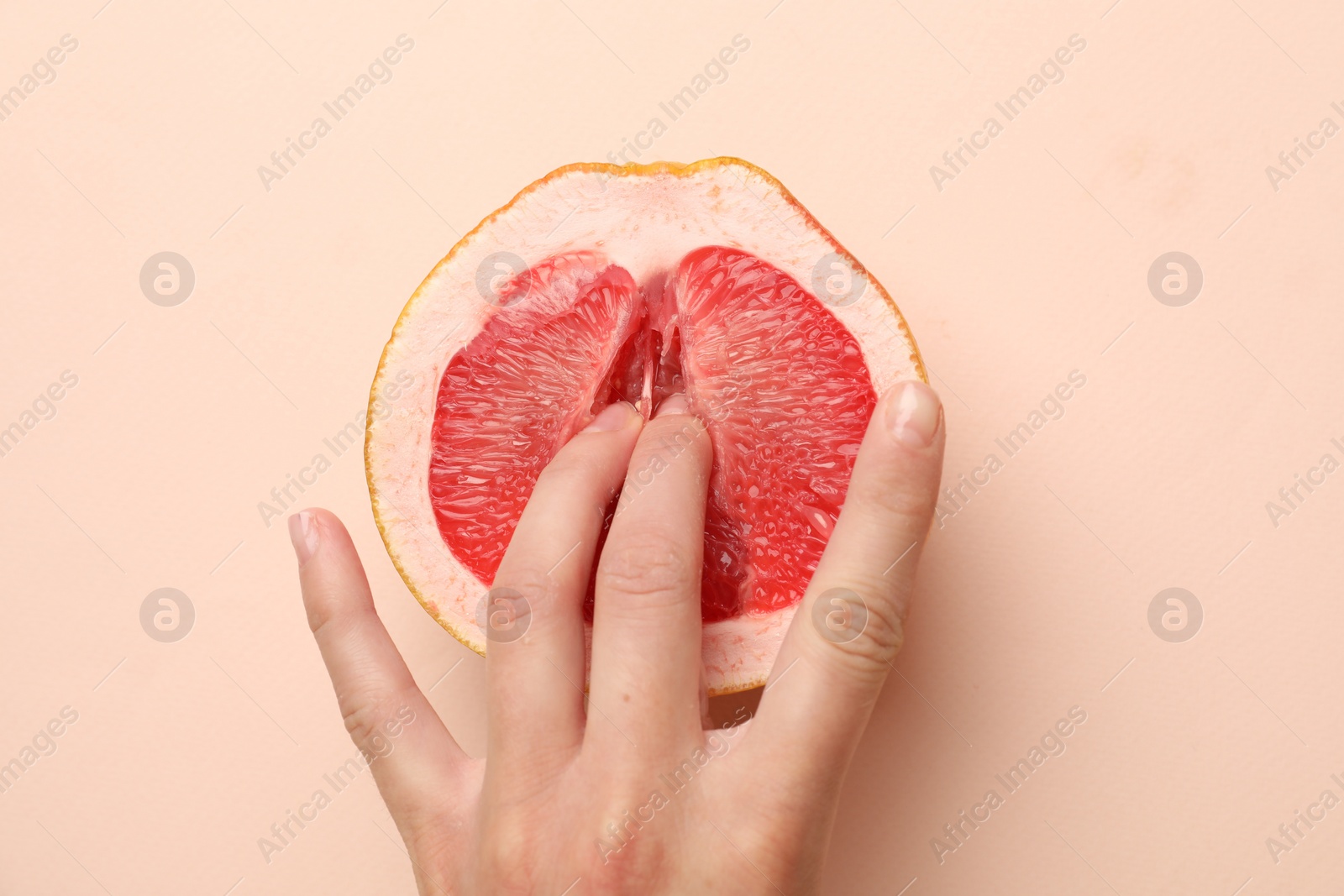 Photo of Woman touching half of grapefruit on beige background, top view. Sex concept