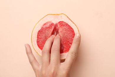 Photo of Woman touching half of grapefruit on beige background, top view. Sex concept