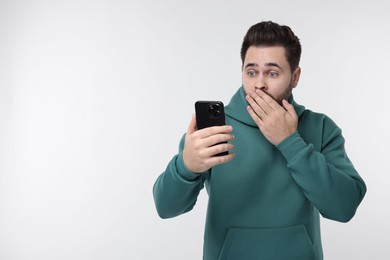 Shocked young man using smartphone on white background, space for text