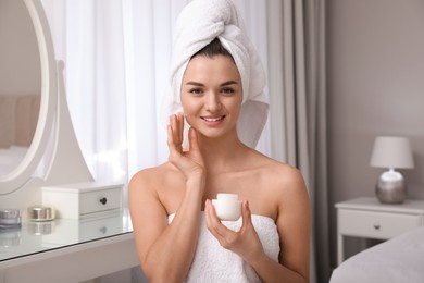 Photo of Beautiful young woman with hair wrapped in towel applying cream at home