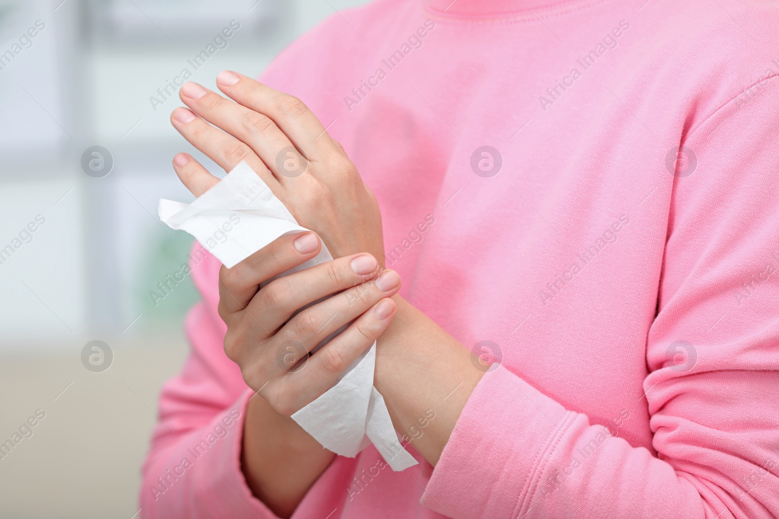 Photo of Woman cleaning hands with paper tissue on blurred background, closeup