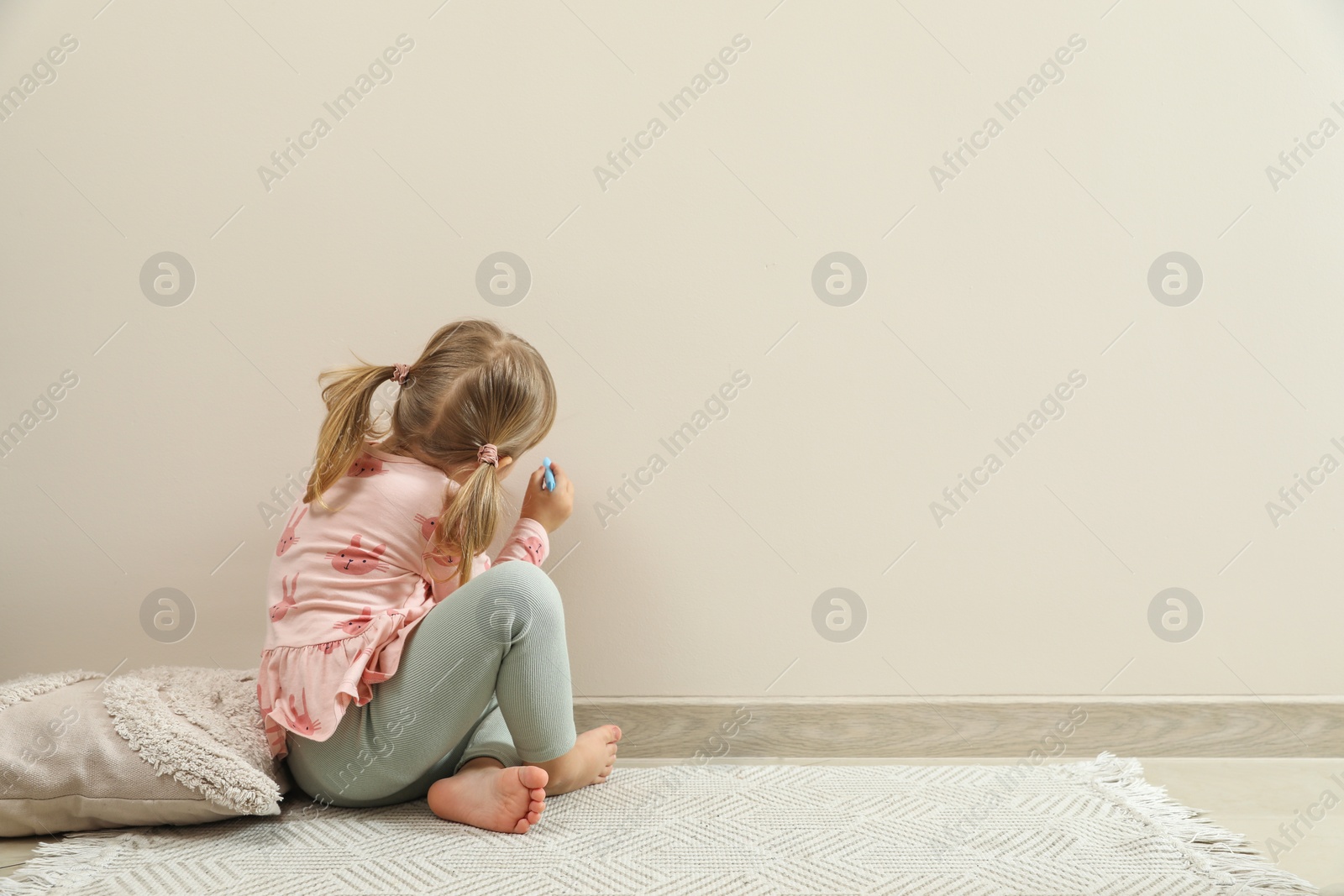 Photo of Little girl drawing on beige wall indoors, back view and space for text. Child`s art