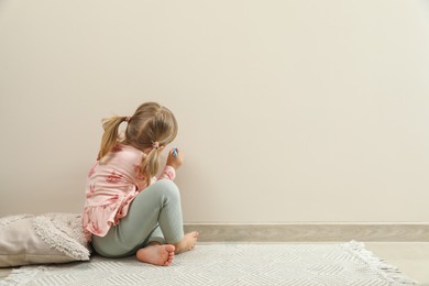 Photo of Little girl drawing on beige wall indoors, back view and space for text. Child`s art