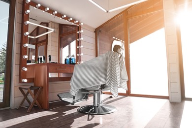 Photo of Stylish hairdresser's workplace with professional armchair and large mirror in barbershop. Interior design