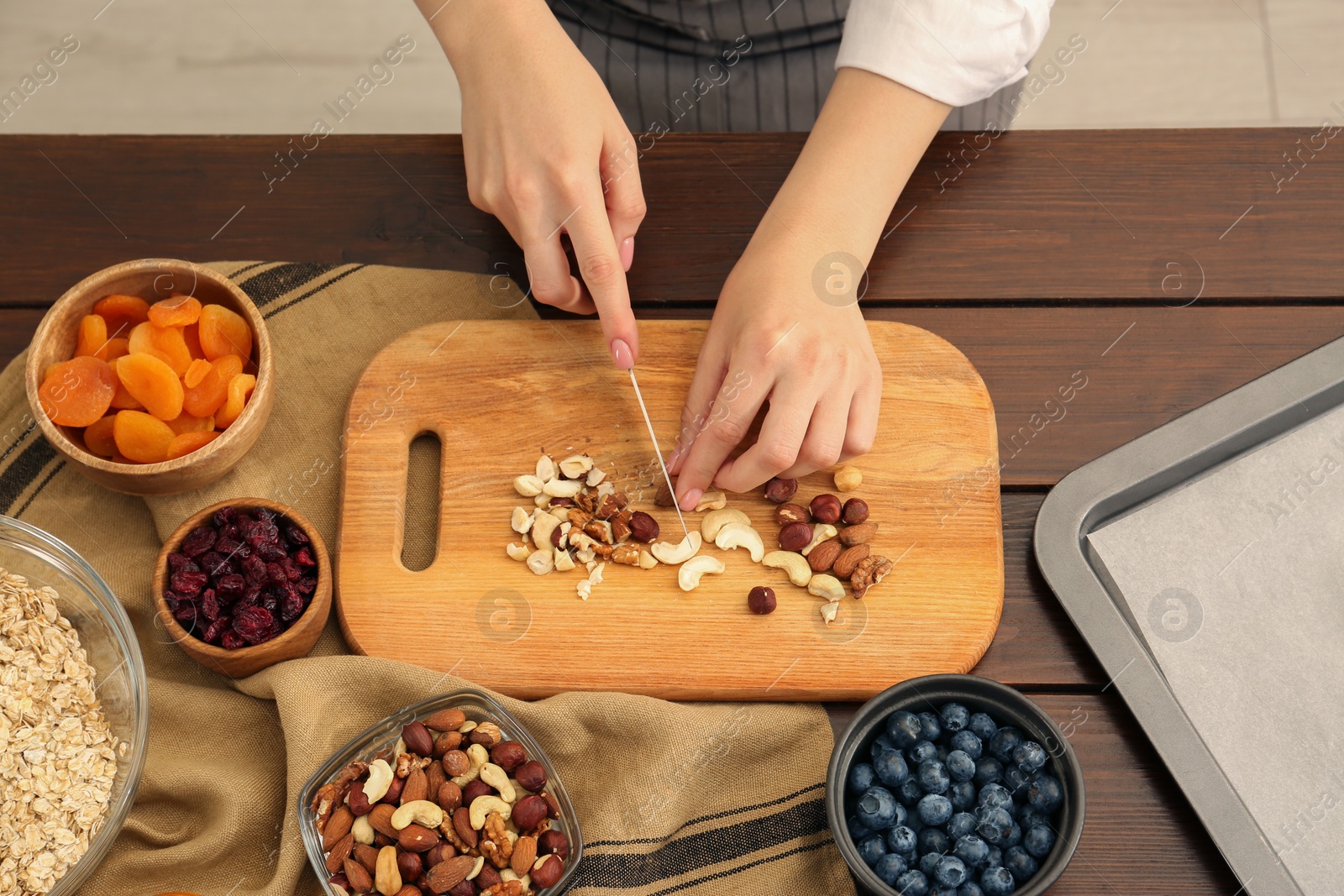 Photo of Making granola. Woman cutting nuts at table in kitchen, top view