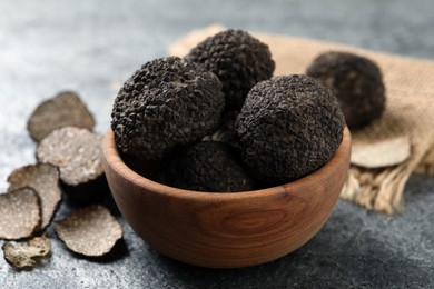 Photo of Black truffles with wooden bowl on grey table, closeup