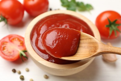 Photo of Taking delicious tomato ketchup with spoon from bowl at white table, closeup