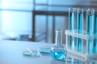 Different glassware and test tubes with light blue liquid on table in laboratory, space for text