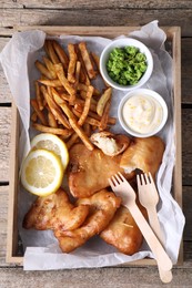 Photo of Tasty fish, chips, sauce and peas on wooden table, top view