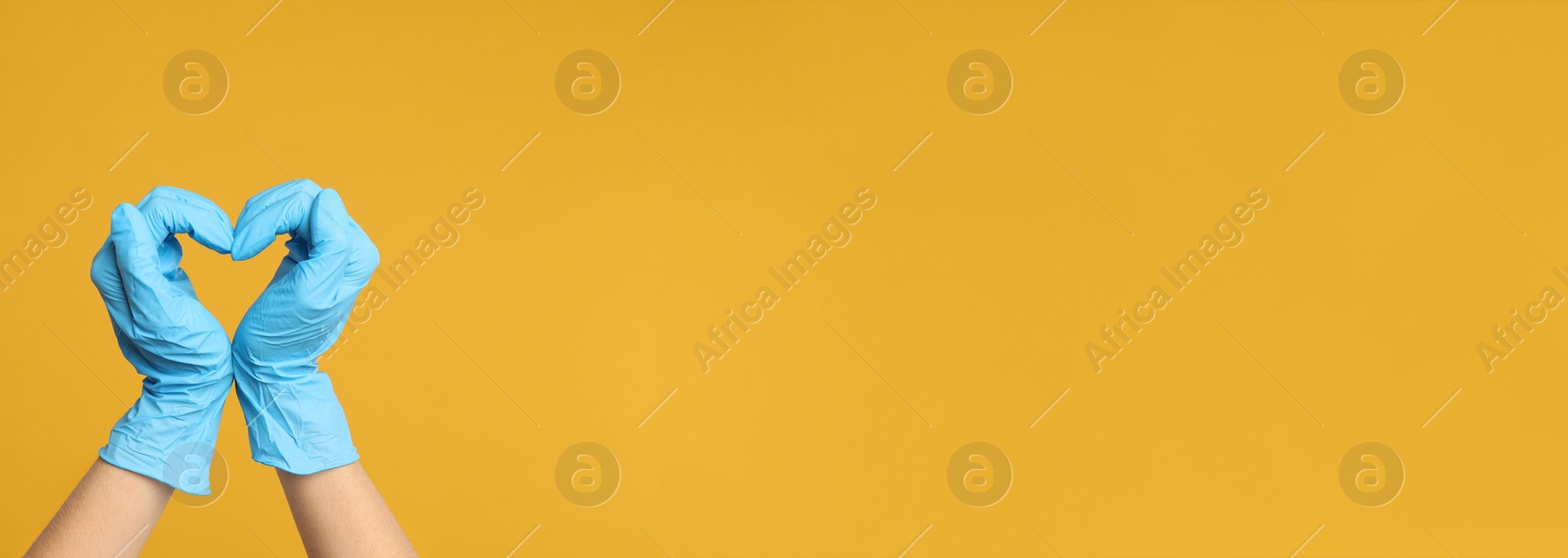 Image of Doctor in medical gloves showing heart with hands on yellow background, closeup. Banner design with space for text 