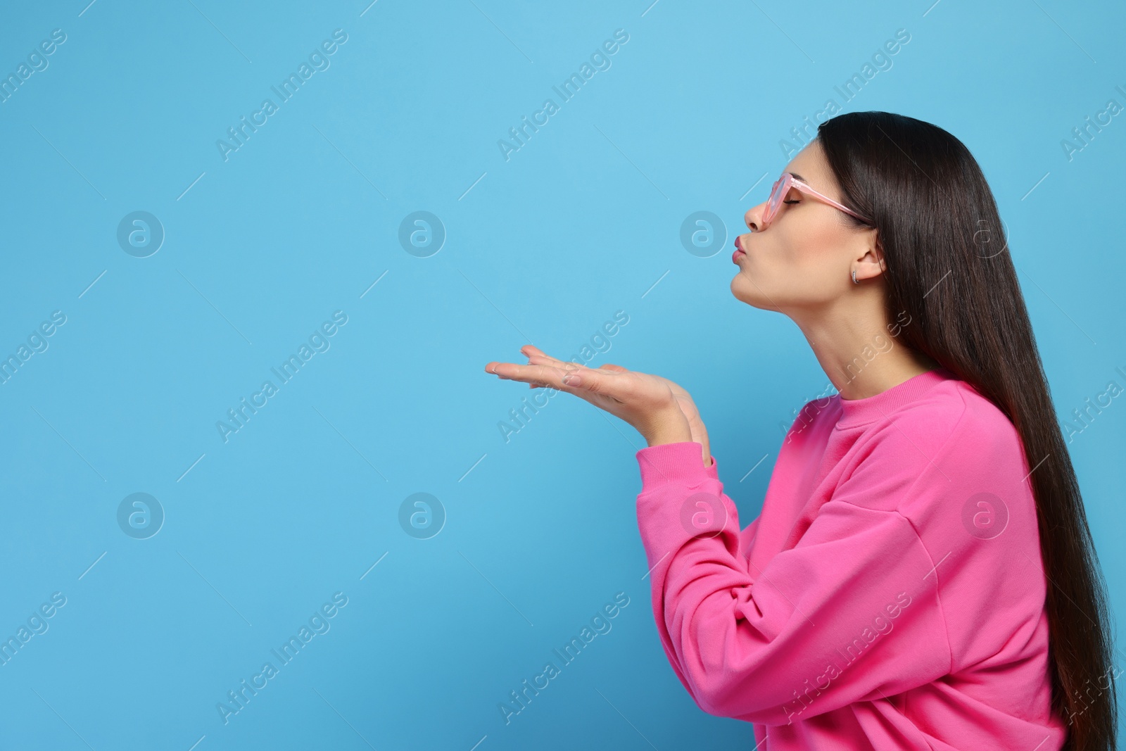 Photo of Beautiful young woman blowing kiss on light blue background. Space for text