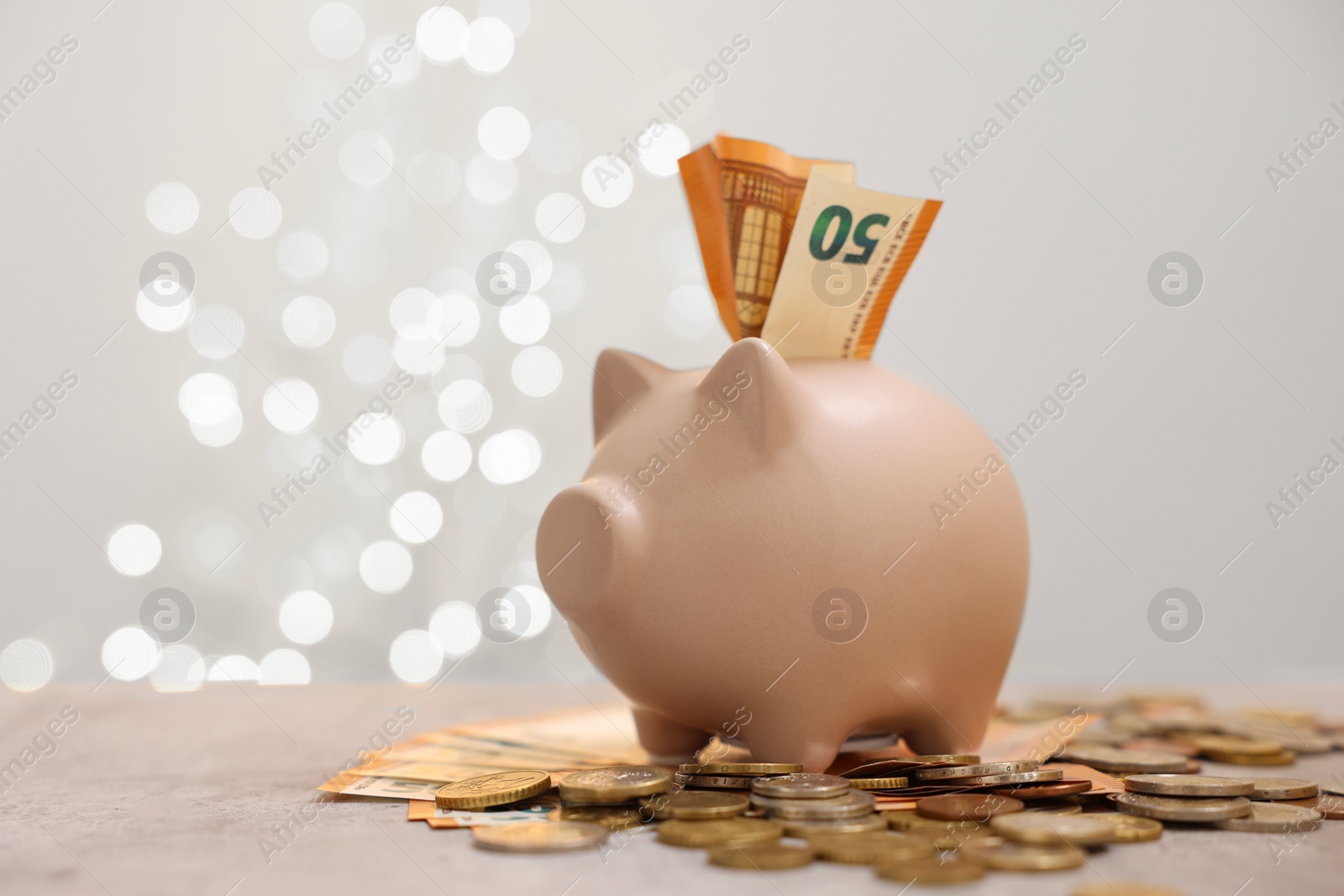 Photo of Piggy bank with euro banknote and coins on grey table against blurred lights