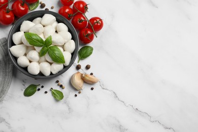 Photo of Delicious mozzarella balls in bowl, tomatoes and basil leaves on white marble table, flat lay. Space for text