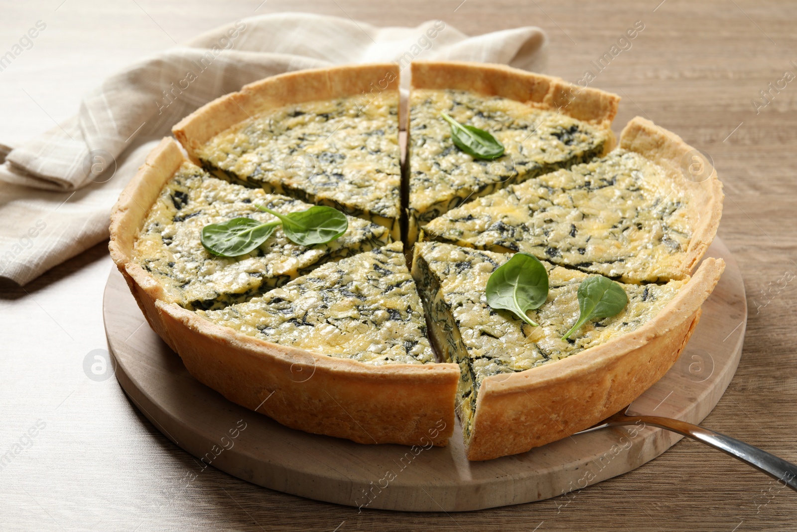 Photo of Cut delicious spinach pie with server on wooden table