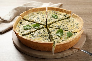 Cut delicious spinach pie with server on wooden table