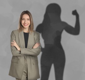 Image of Businesswoman and shadow of strong muscular lady behind her on grey wall. Concept of inner strength
