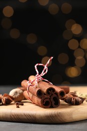 Cinnamon sticks and other spices on table against black background with blurred lights, closeup