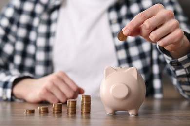 Photo of Financial savings. Man putting coin into piggy bank at wooden table, closeup