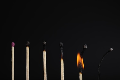 Photo of Row of burnt matches and whole one on black background