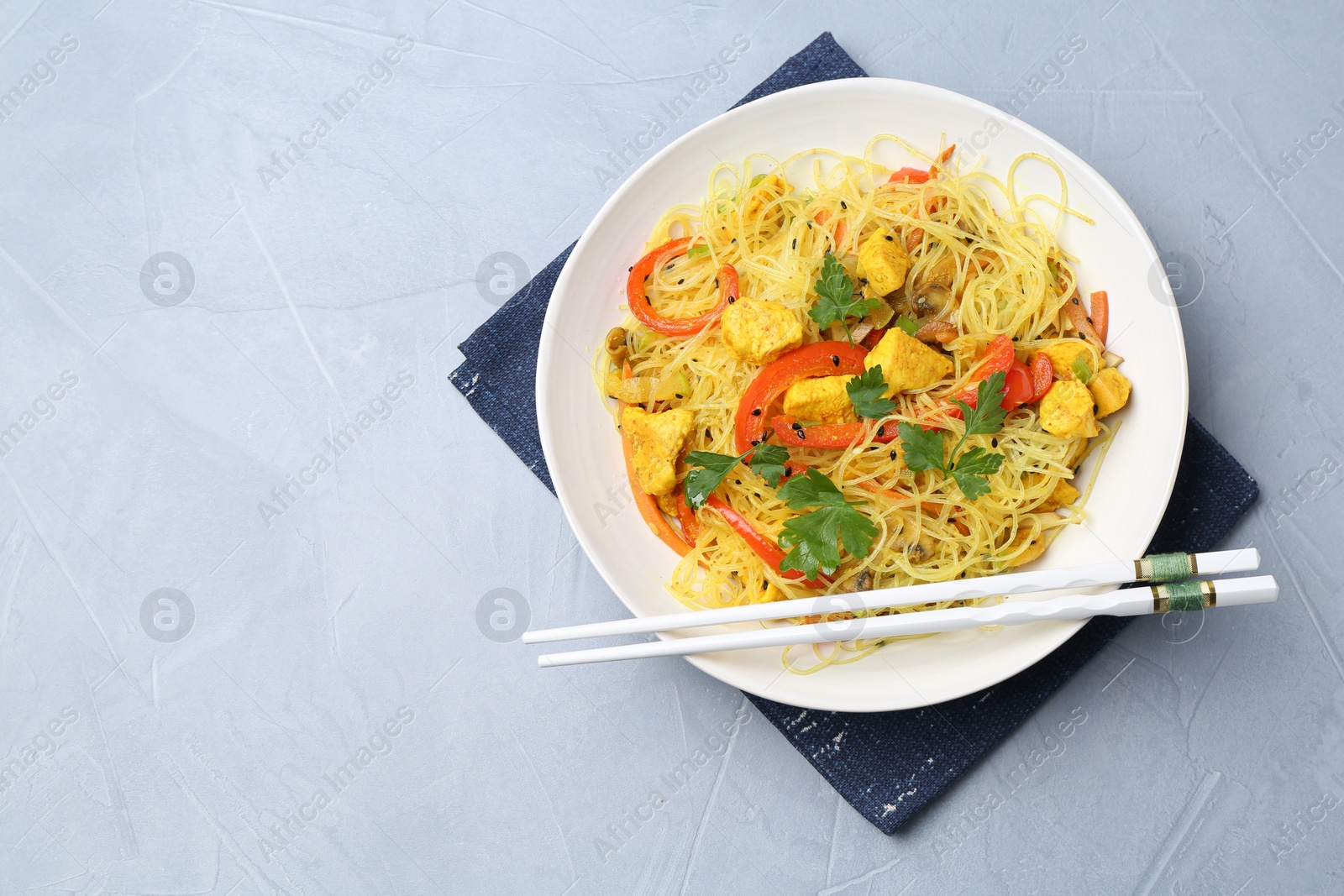 Photo of Stir-fry. Delicious cooked noodles with chicken and vegetables in bowl served on gray textured table, top view. Space for text