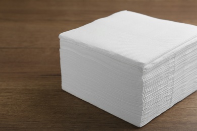 Photo of Stack of white clean paper tissues on wooden table, closeup