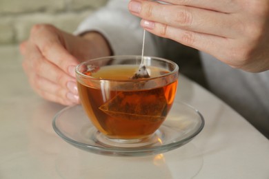 Photo of Woman taking tea bag out of cup at table indoors, closeup