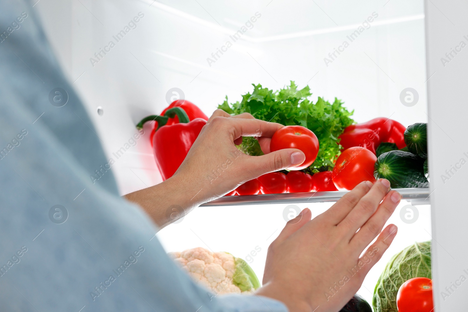 Photo of Young woman taking tomato out of refrigerator, closeup
