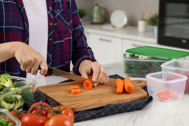 Photo of Woman cutting carrot near containers with fresh products on white marble table in kitchen, closeup. Food storage