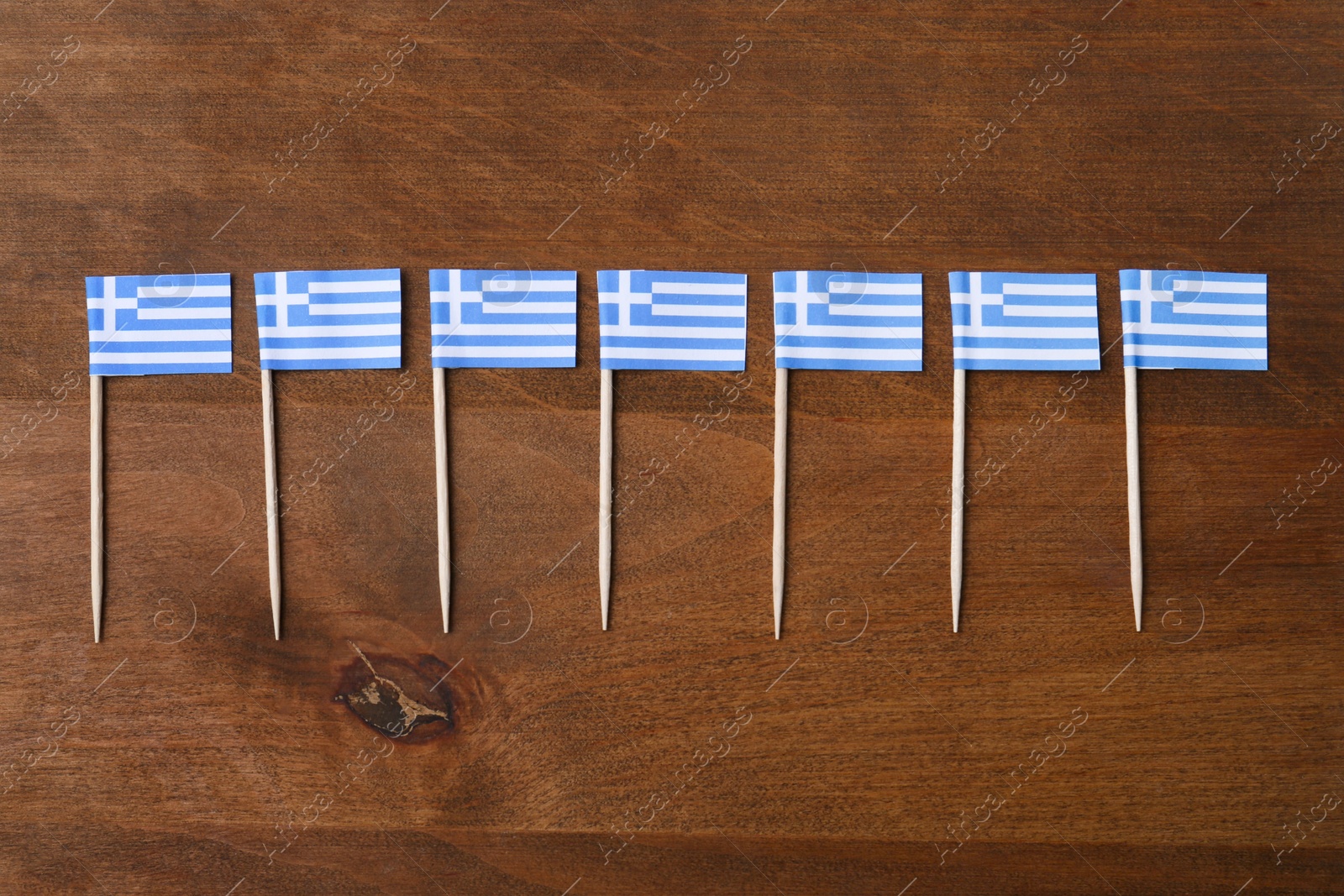 Photo of Small paper flags of Greece on wooden table, flat lay