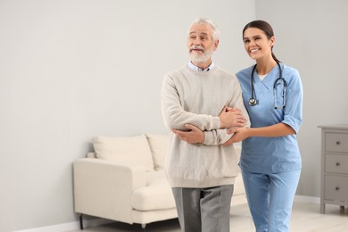 Smiling nurse supporting elderly patient in hospital. Space for text