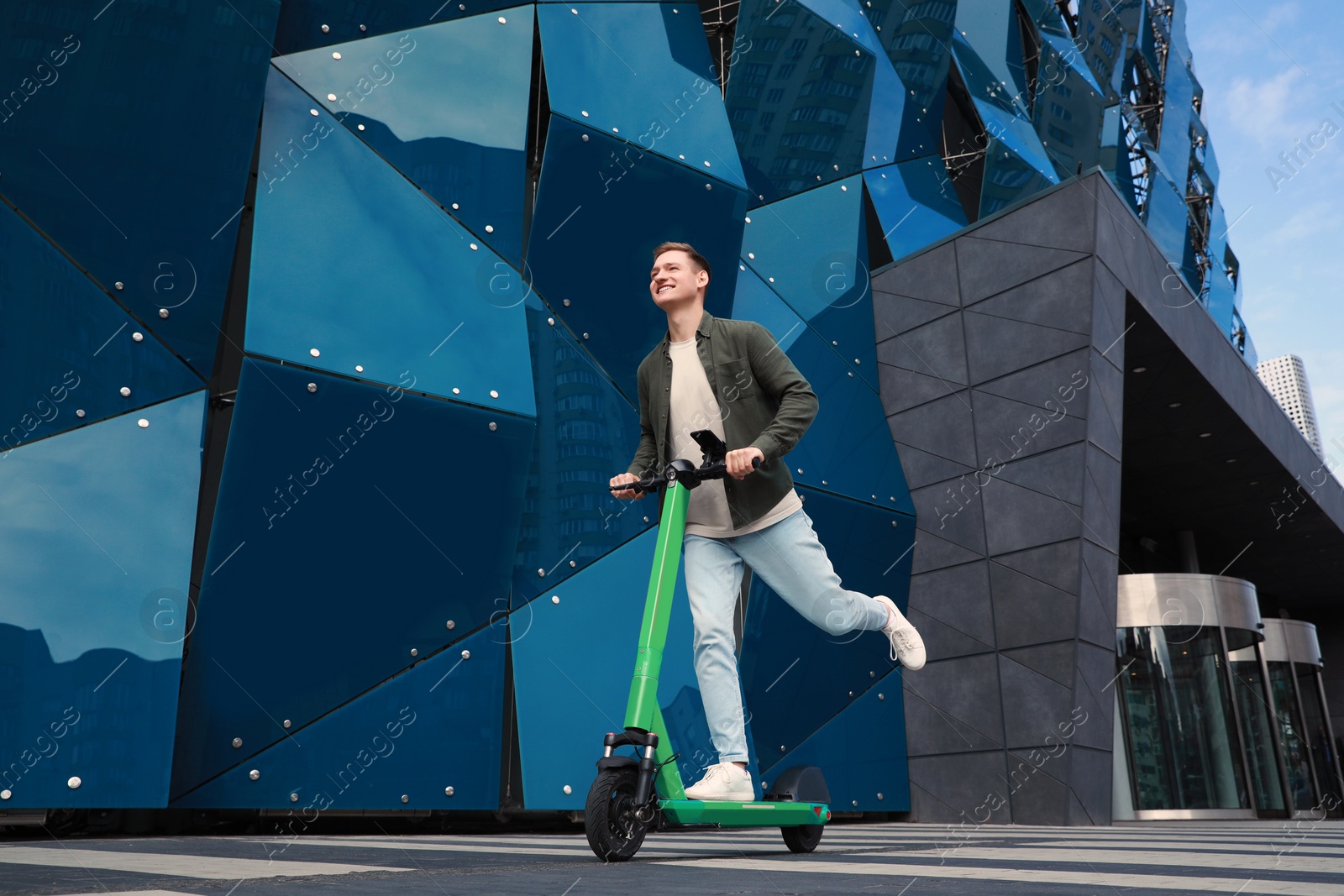 Photo of Happy man riding modern electric kick scooter on city street