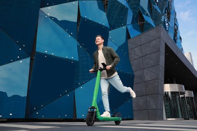 Happy man riding modern electric kick scooter on city street