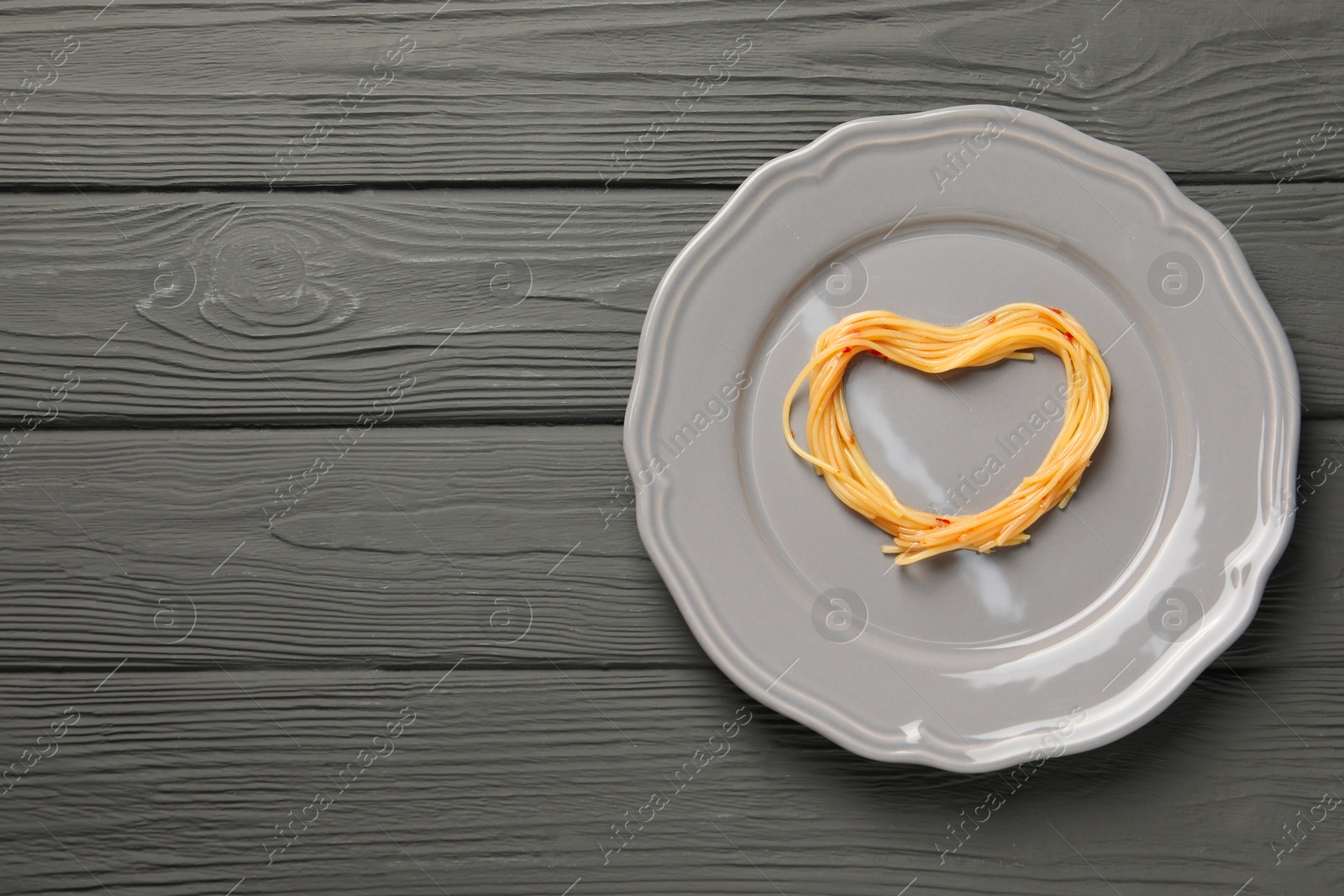 Photo of Heart made with spaghetti on grey wooden table, top view. Space for text