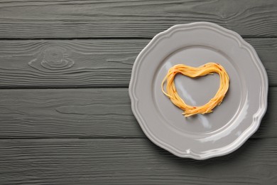 Heart made with spaghetti on grey wooden table, top view. Space for text