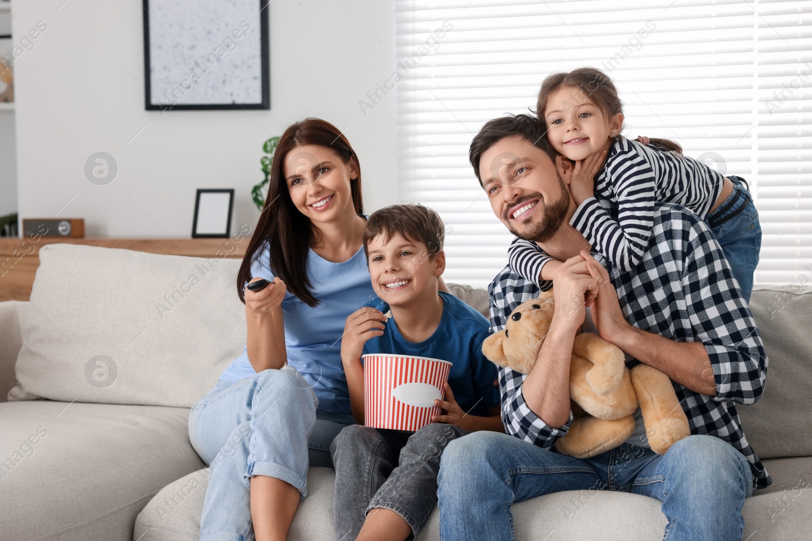 Photo of Happy family watching movie at home. Mother changing TV channels with remote control