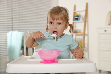 Photo of Cute little child eating tasty yogurt with spoon at home