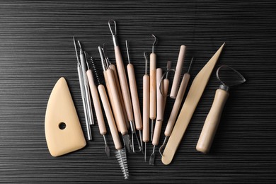 Clay and set of modeling tools on dark gray wooden table, flat lay