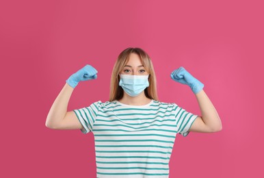 Photo of Woman with protective mask and gloves showing muscles on pink background. Strong immunity concept