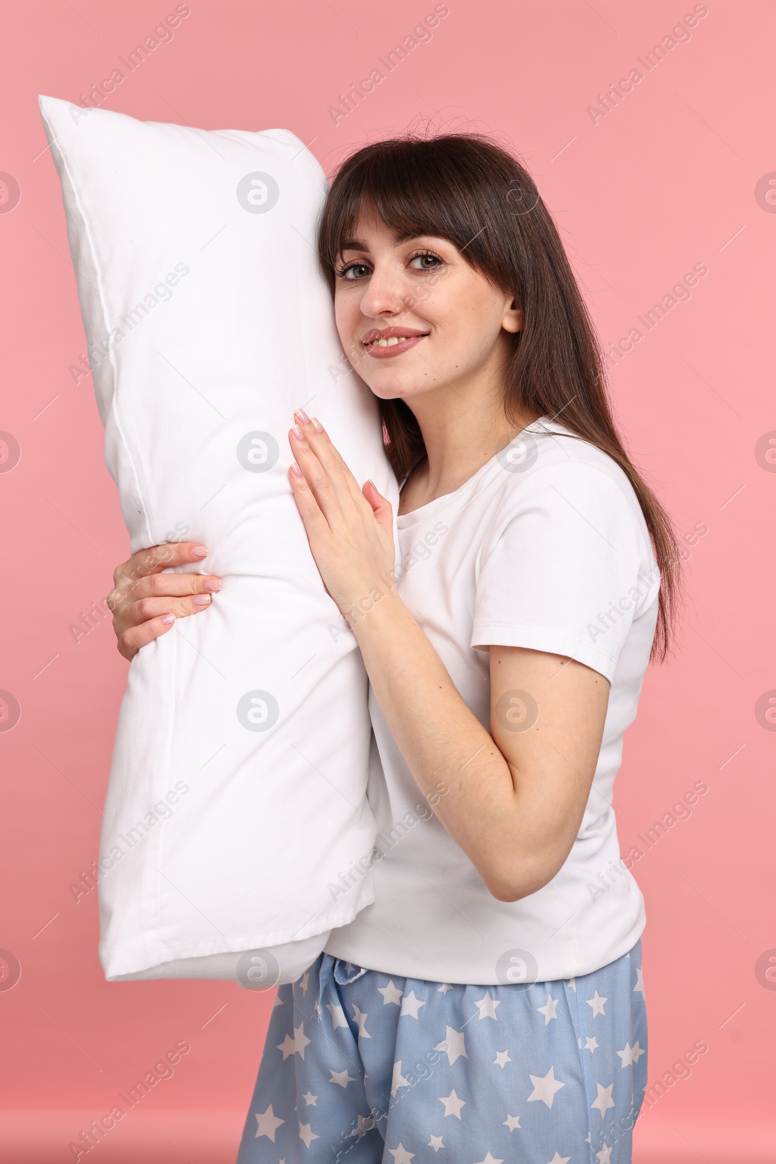 Photo of Happy woman in pyjama holding pillow on pink background