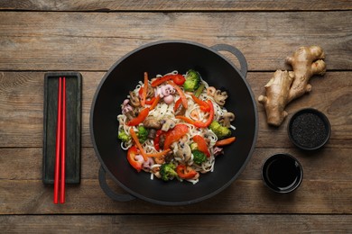 Photo of Stir fried noodles with seafood and vegetables in wok on wooden table, flat lay