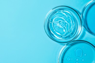 Petri dishes with liquids on light blue background, flat lay. Space for text