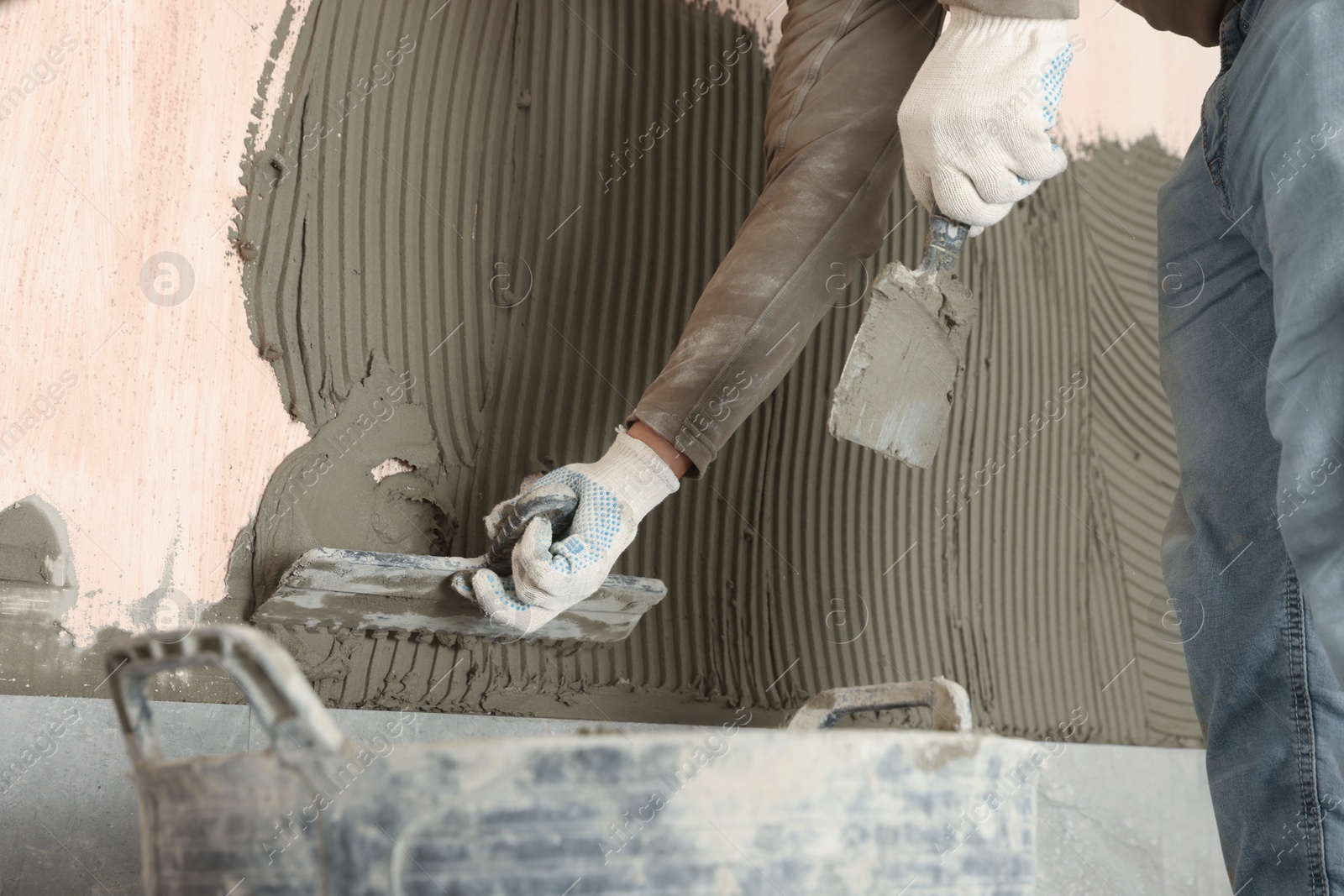 Photo of Worker applying cement on wall for tile installation, closeup