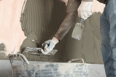 Photo of Worker applying cement on wall for tile installation, closeup