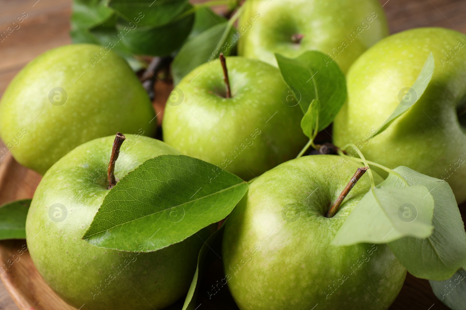 Photo of Fresh ripe green apples and leaves on wooden plate, closeup