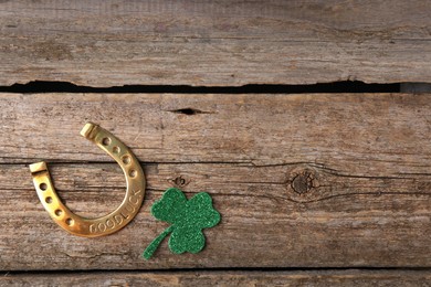 St. Patrick's day. Golden horseshoe and green decorative clover leaf on wooden table, flat lay. Space for text